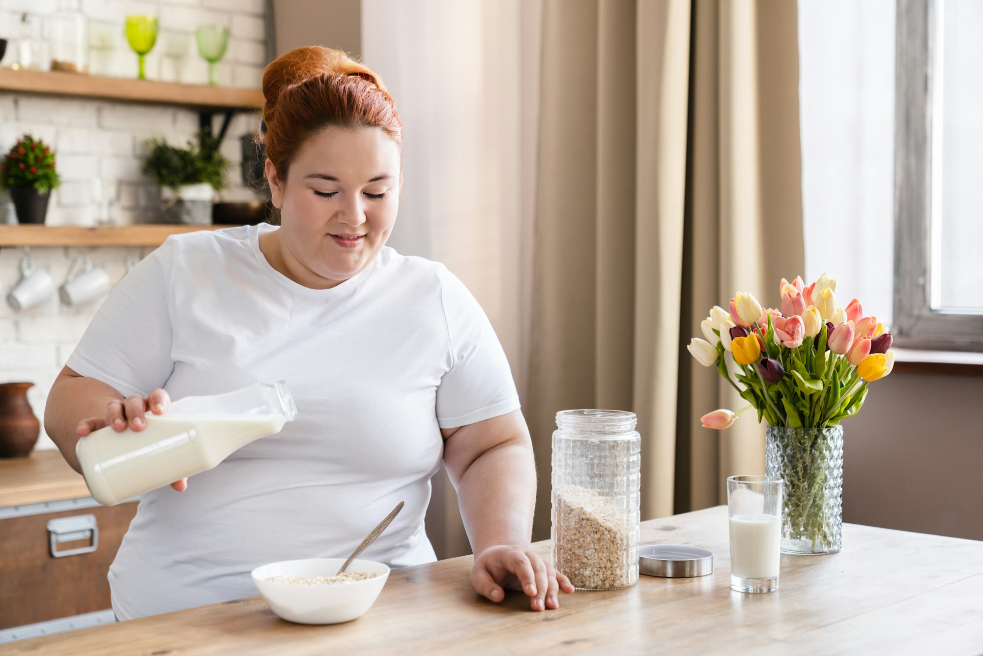 Caucasian plus size fat woman eating oat-flakes in the kitchen for breakfast.
